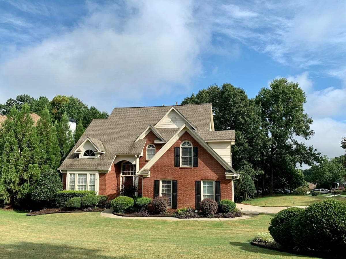 Red-brick colonial with a steep replaced roof under a broken Kansas sky